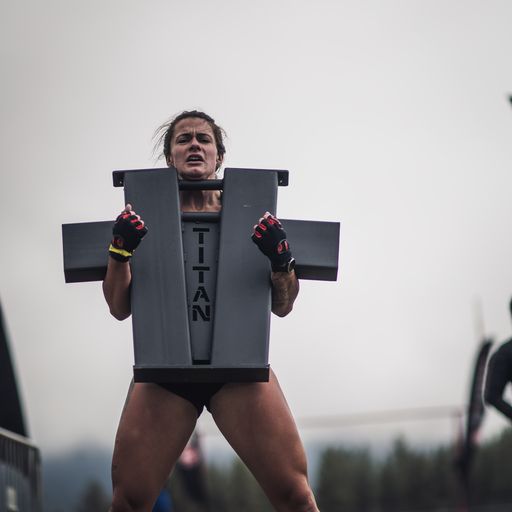 A woman carries a metal object during a Spartan Race. The object says 'TITAN' on it.